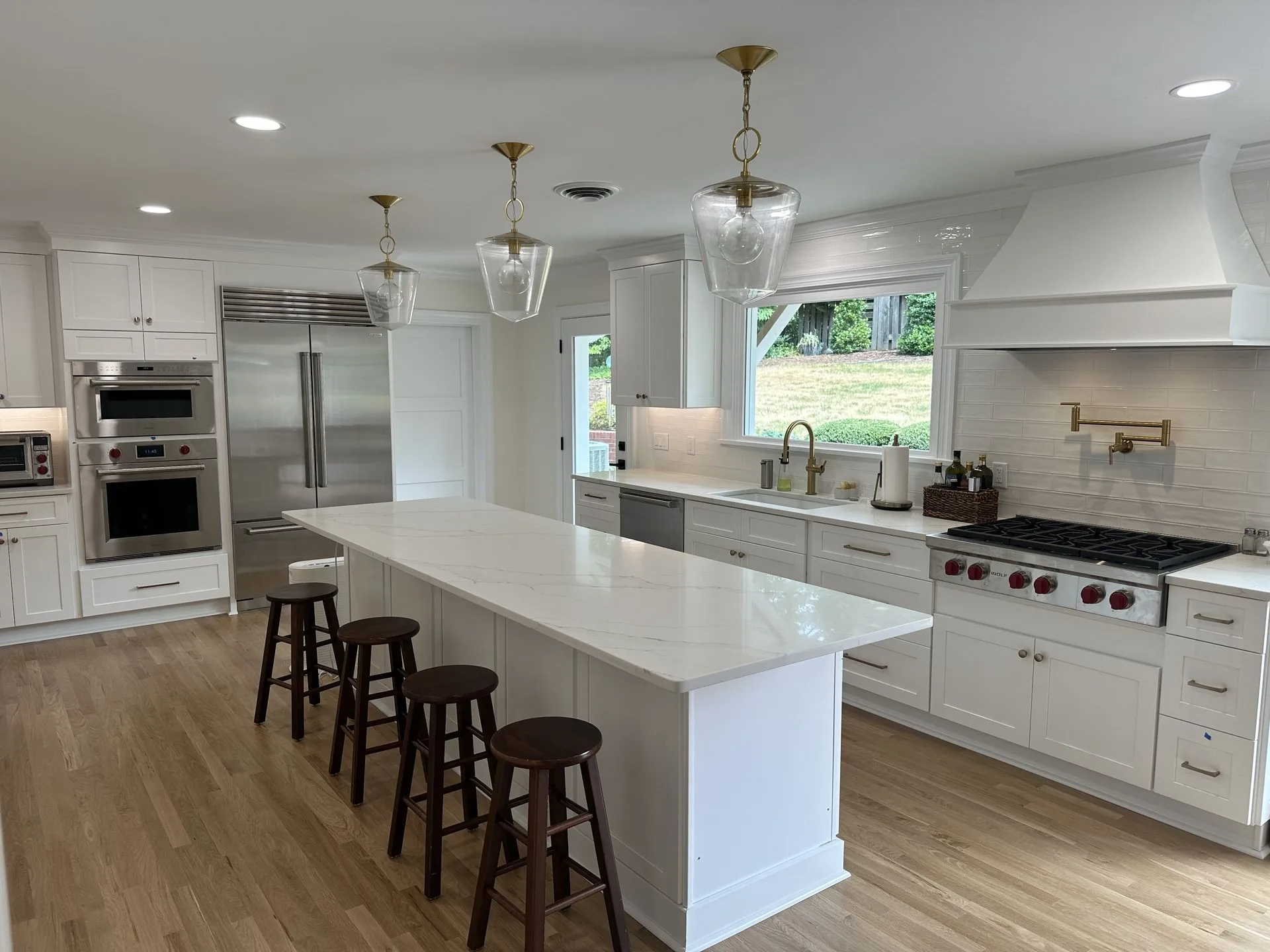 Remodeled kitchen in Richmond, VA by Swift Run Renovations. White cabinetry, quartz island, and brass pendant lighting