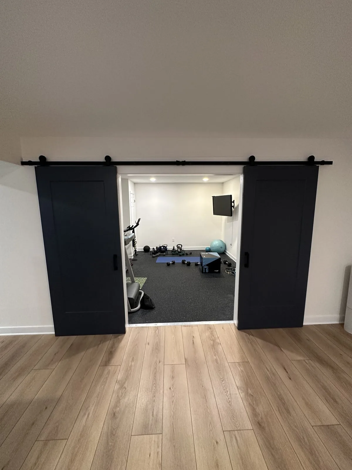 Finished basement with a home gym set behind custom barn doors. Lake Summer Mews, Richmond, VA